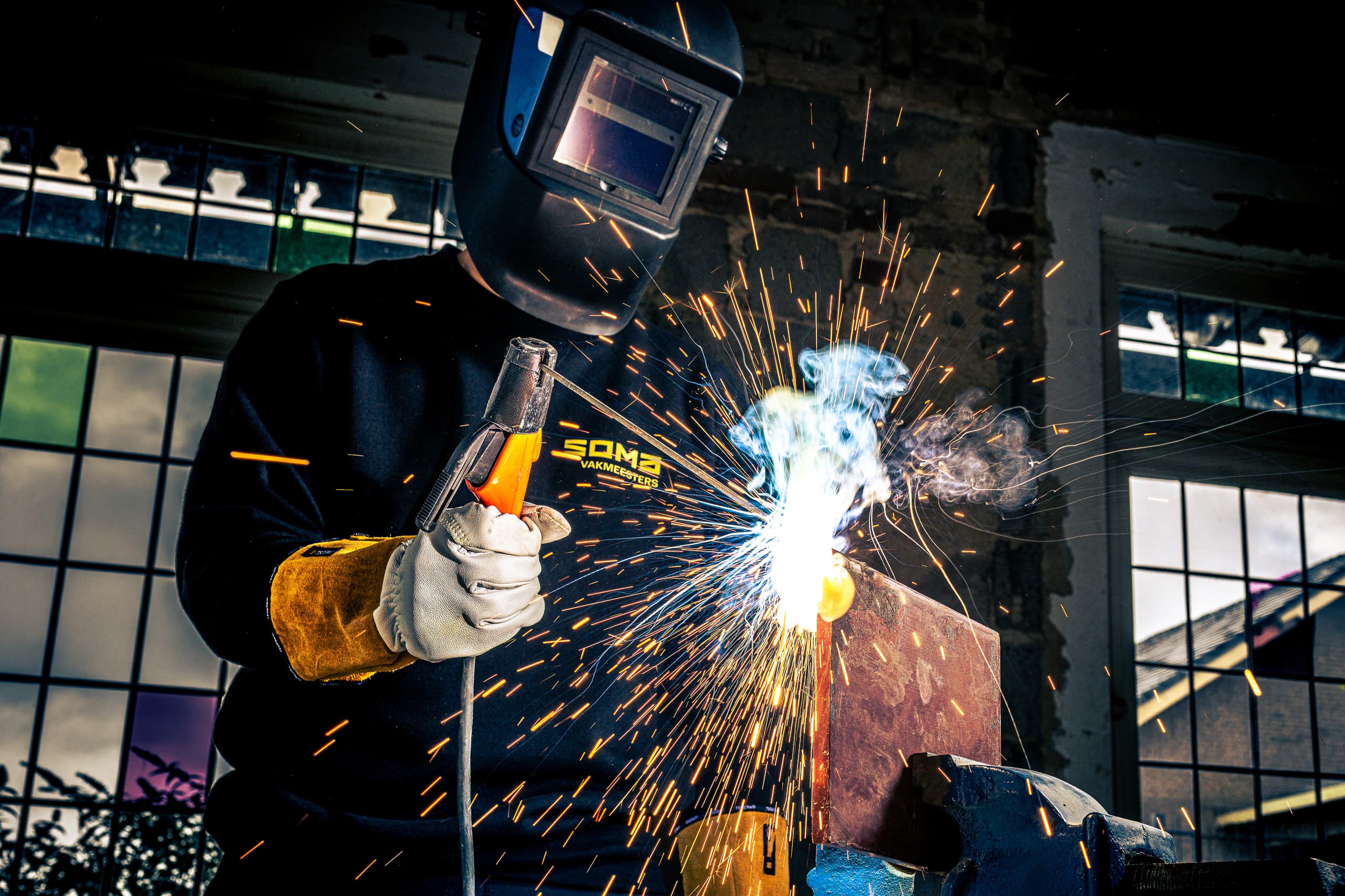 Lasser van SOMA Vakmeesters aan het werk, de vonken slaan van het staal in een fabriekshal