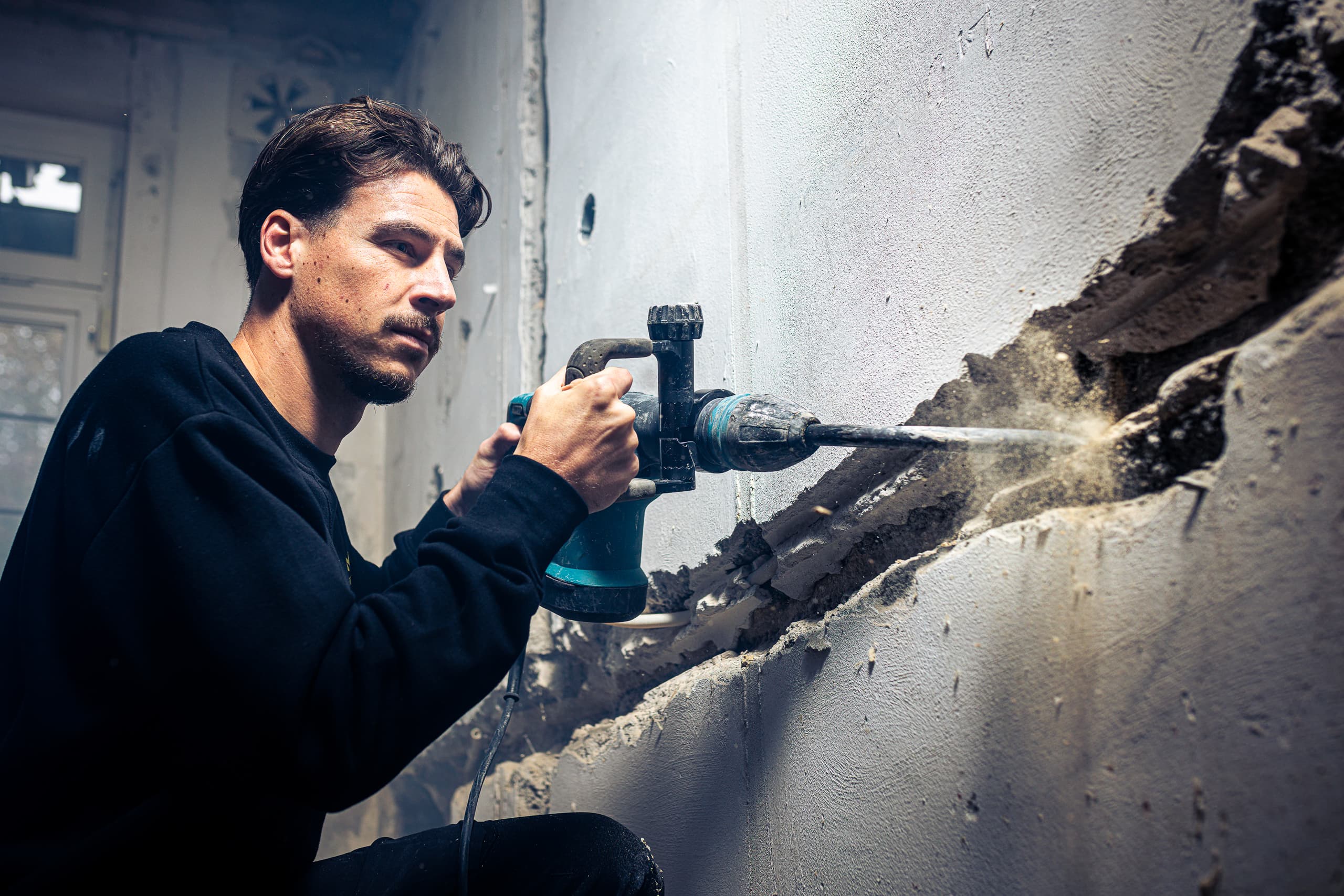 Vakman hakt met een breekhamer oud pleisterwerk van een muur