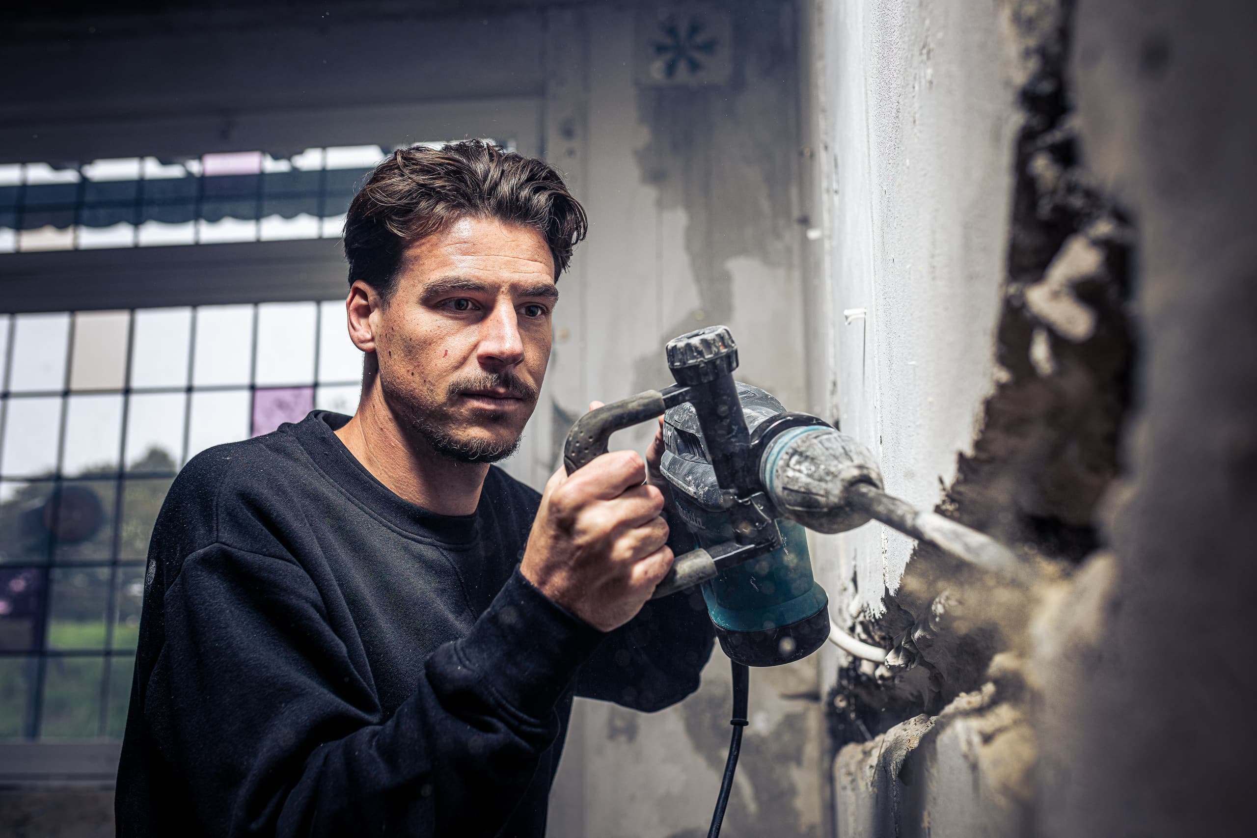 Vakman van SOMA Vakmeesters hakt met een breekhamer een sleuf in een oude muur