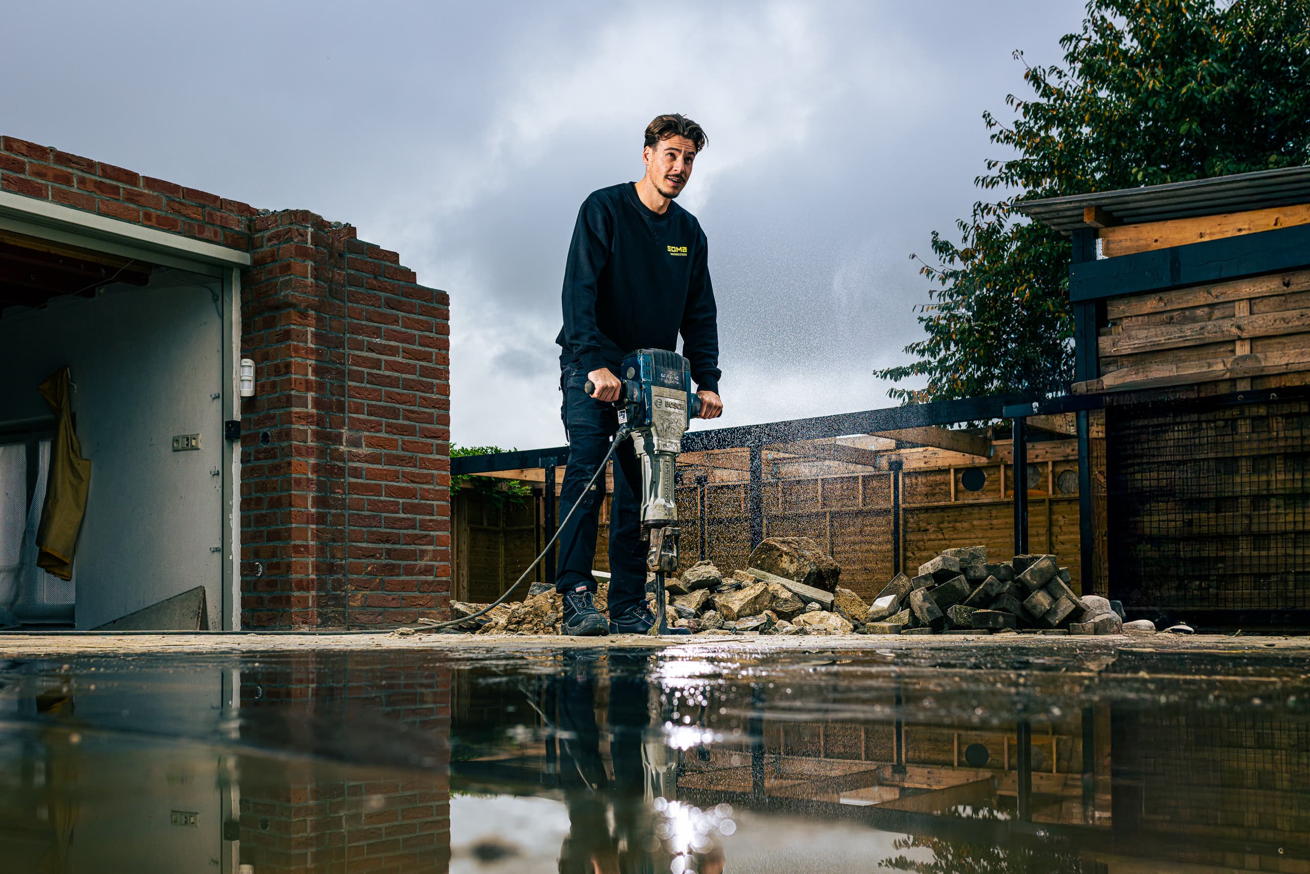 Vakman van SOMA Vakmeesters breekt met een sloophamer de bestrating naast een woning open